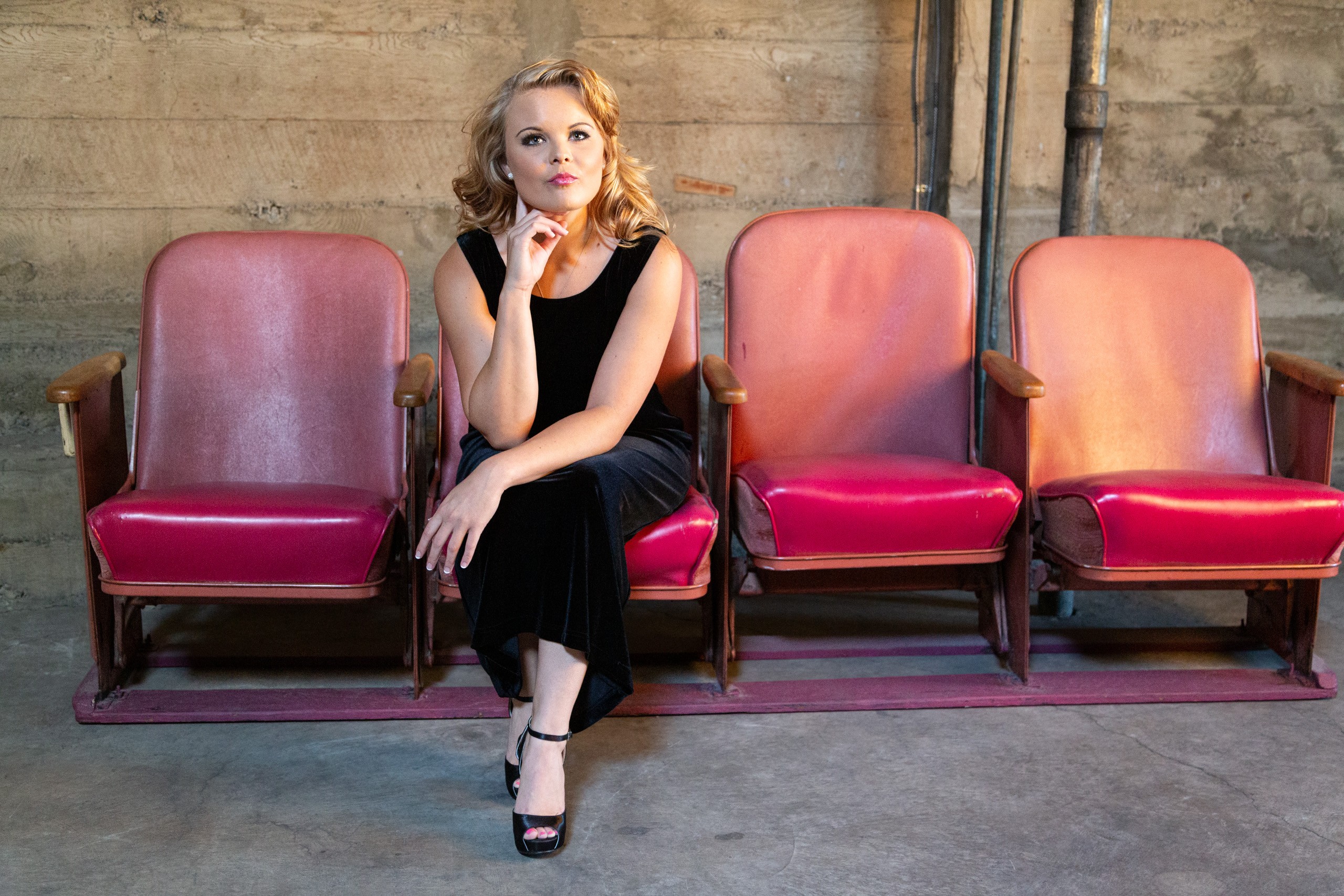 Woman in black dress seated on vintage theater chair, thoughtful pose