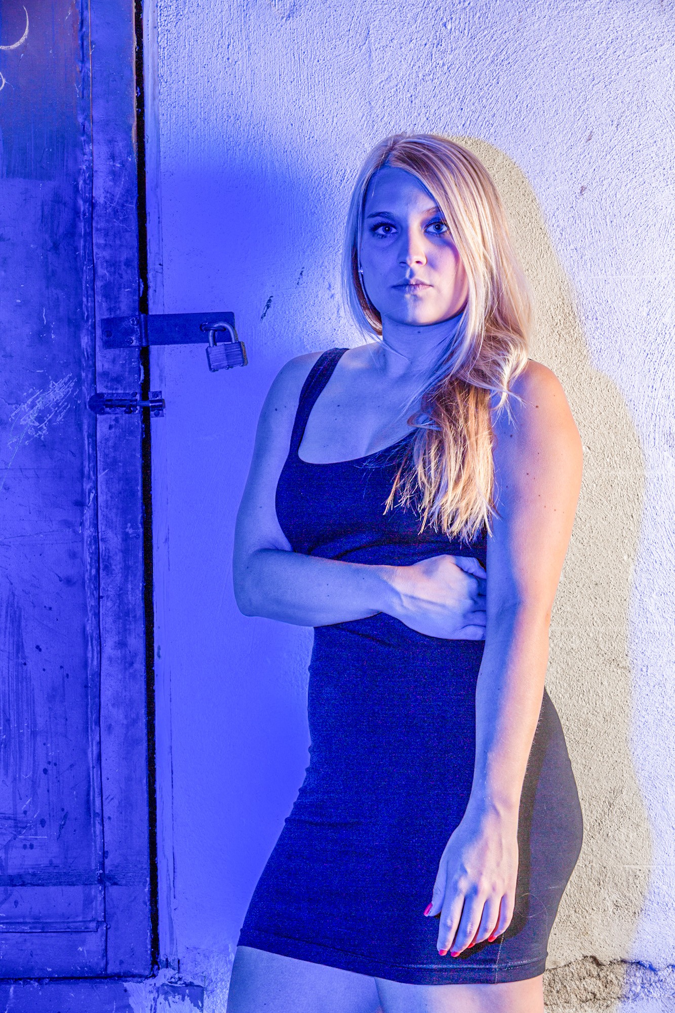 Woman in black dress posed against blue door and textured wall