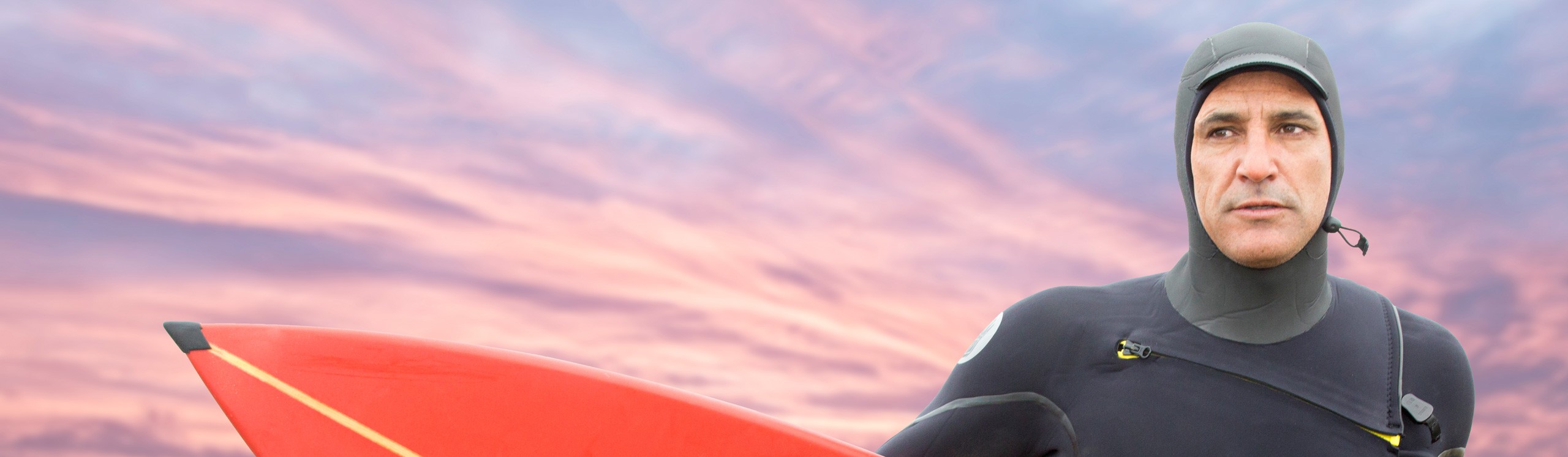 Surfer in wetsuit holding red surfboard at sunset