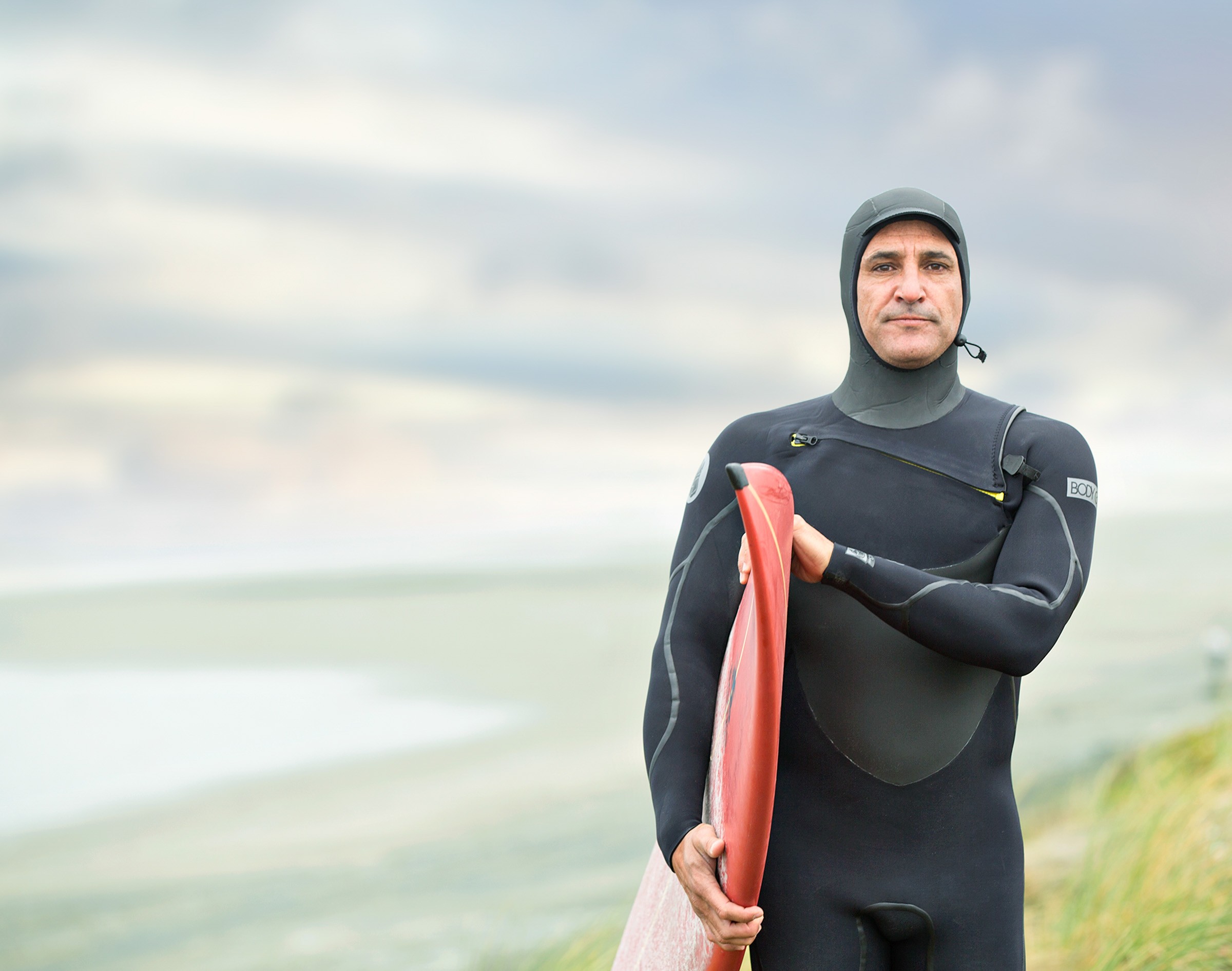 Surfer in wetsuit holding red board by ocean shore