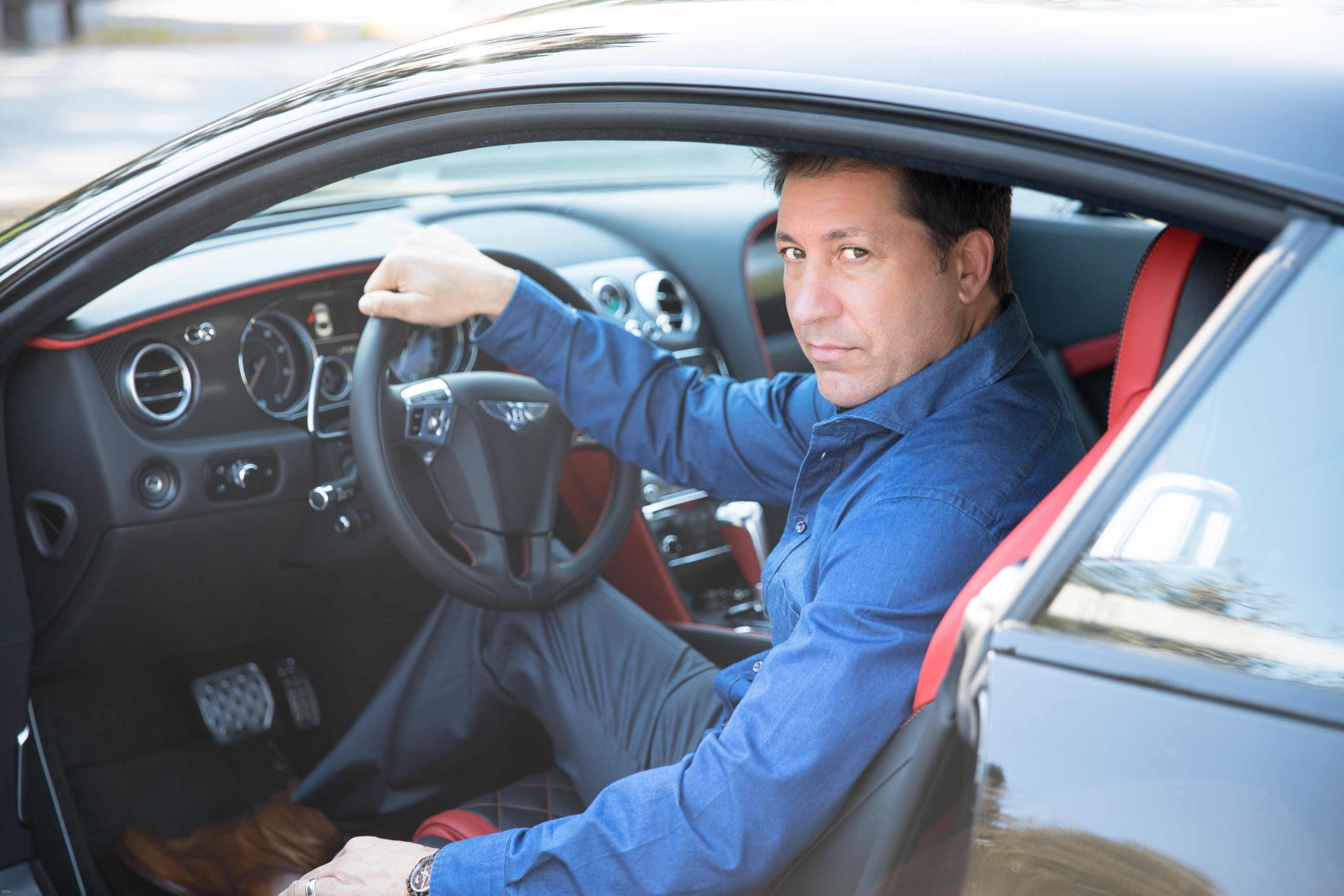 Man in blue shirt sitting in sports car with red interior