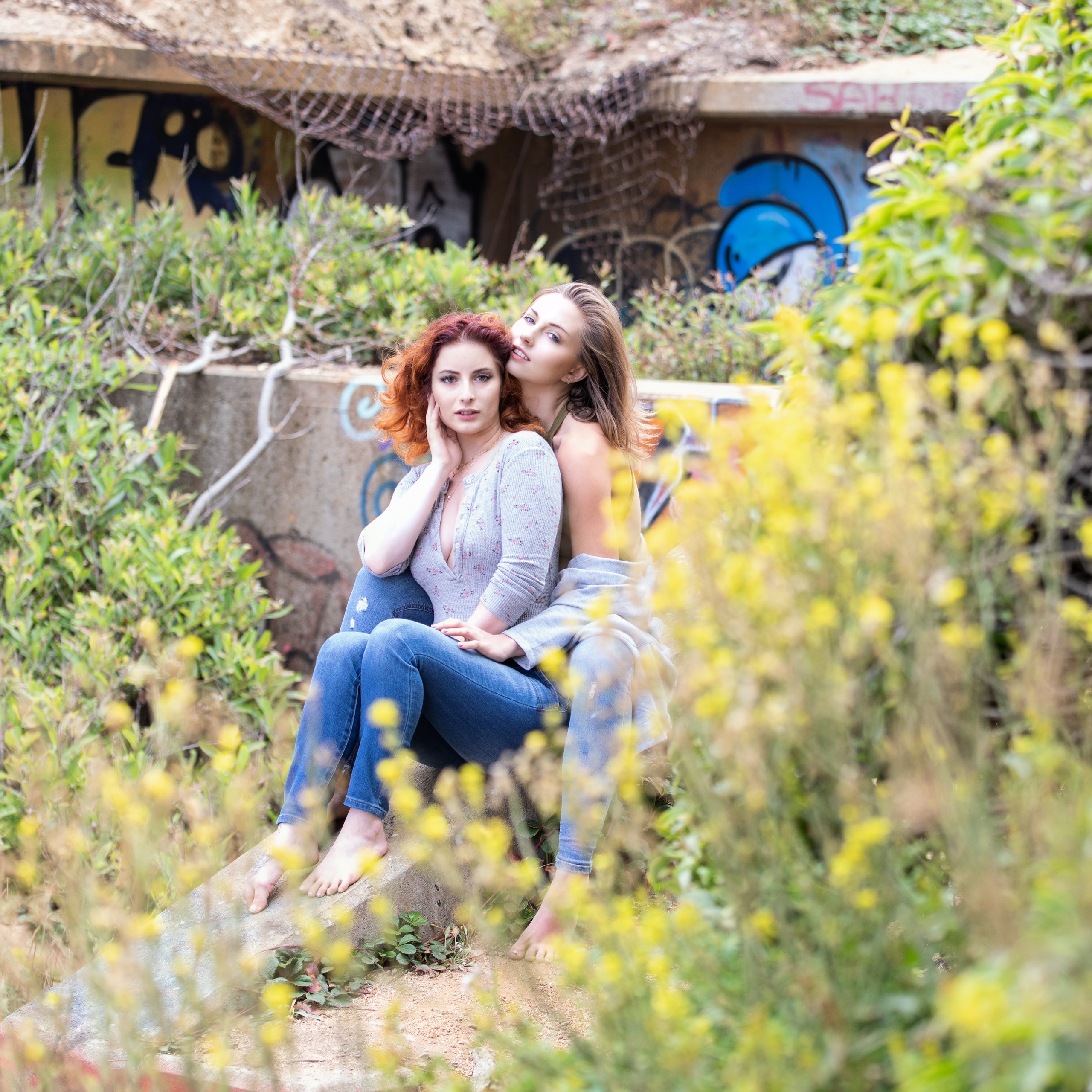 Two women posing together among yellow wildflowers and urban ruins