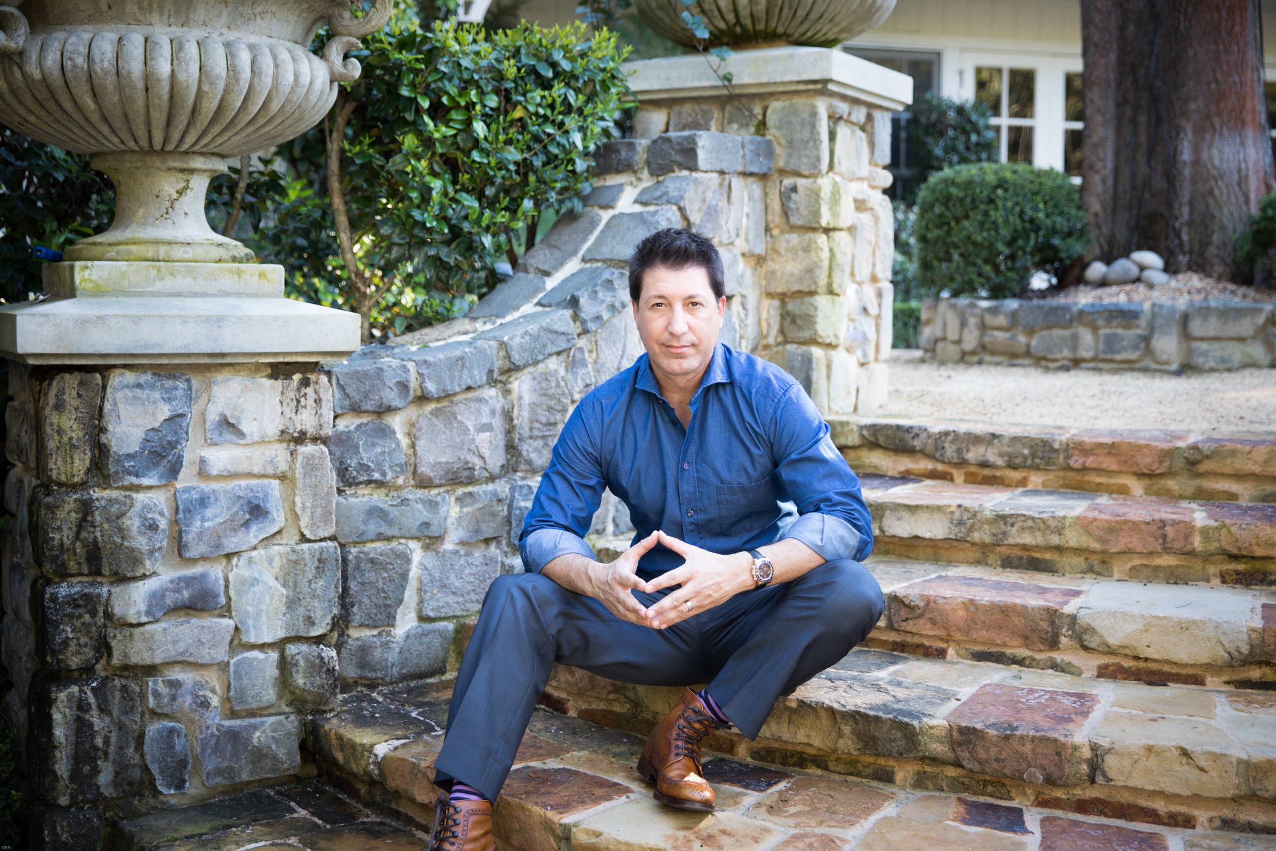 Professional man crouches on stone steps in elegant garden setting