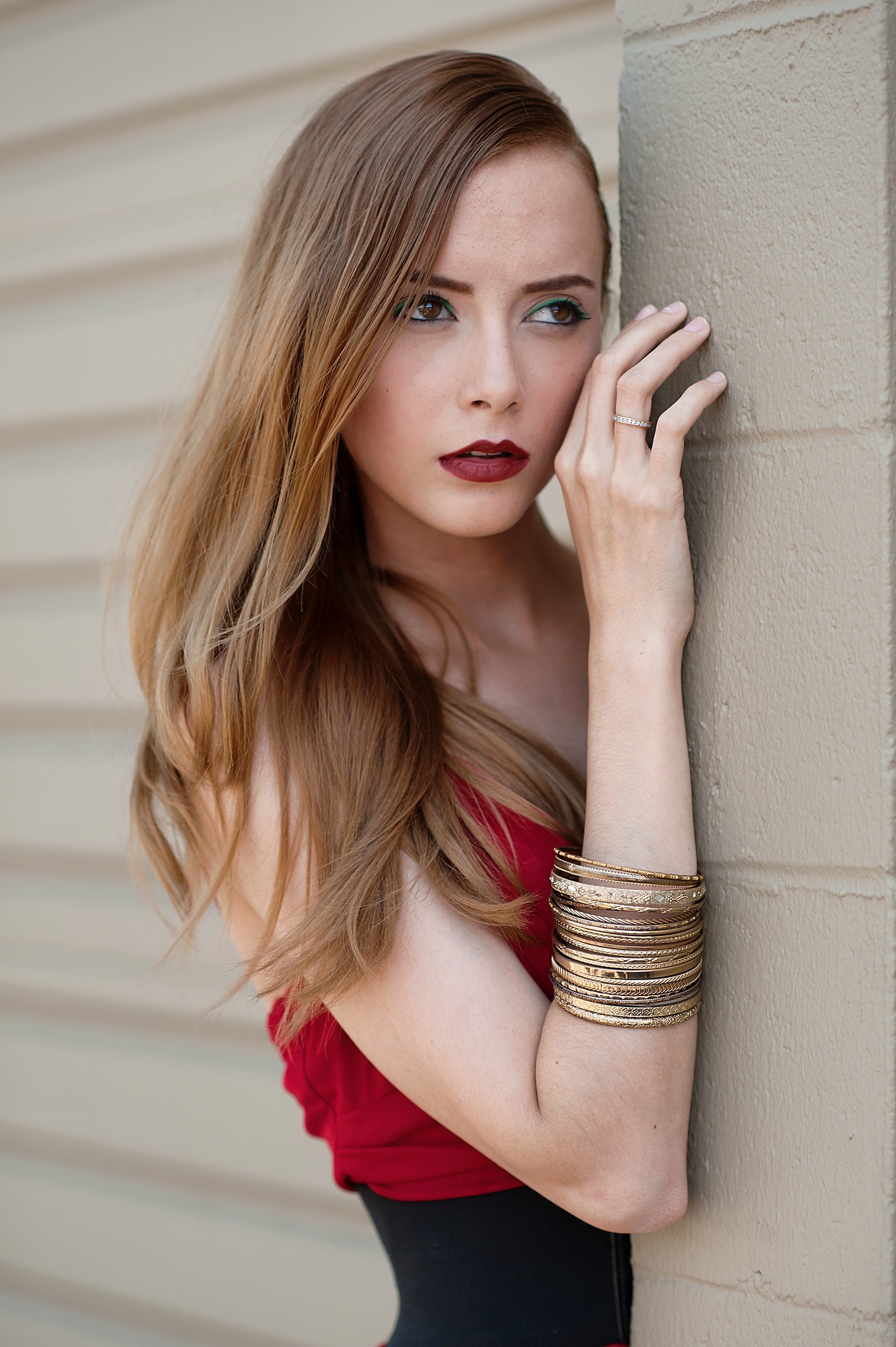 Woman in red top leaning against textured wall, elegant portrait