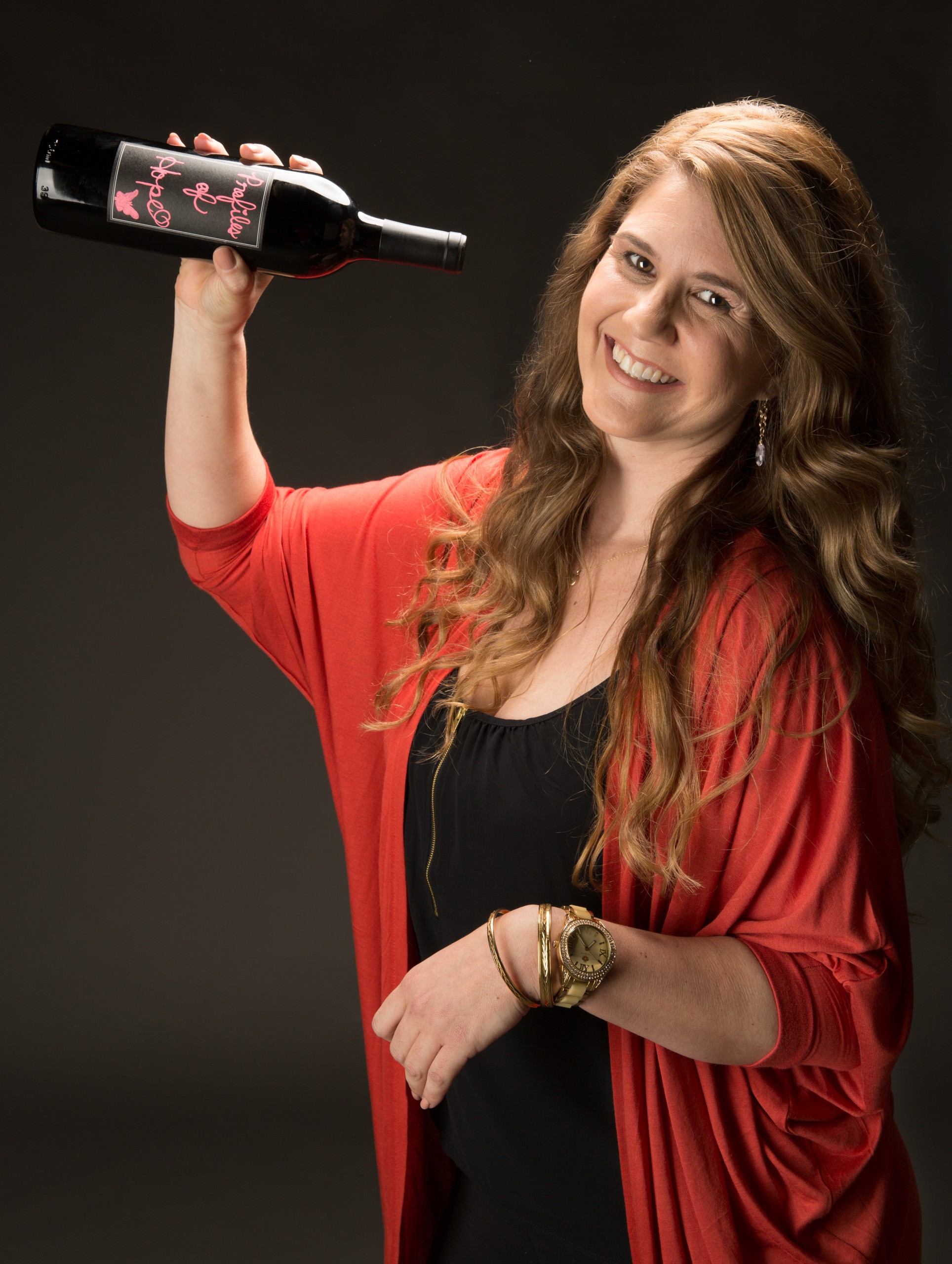 Woman in red cardigan holding wine bottle against black background