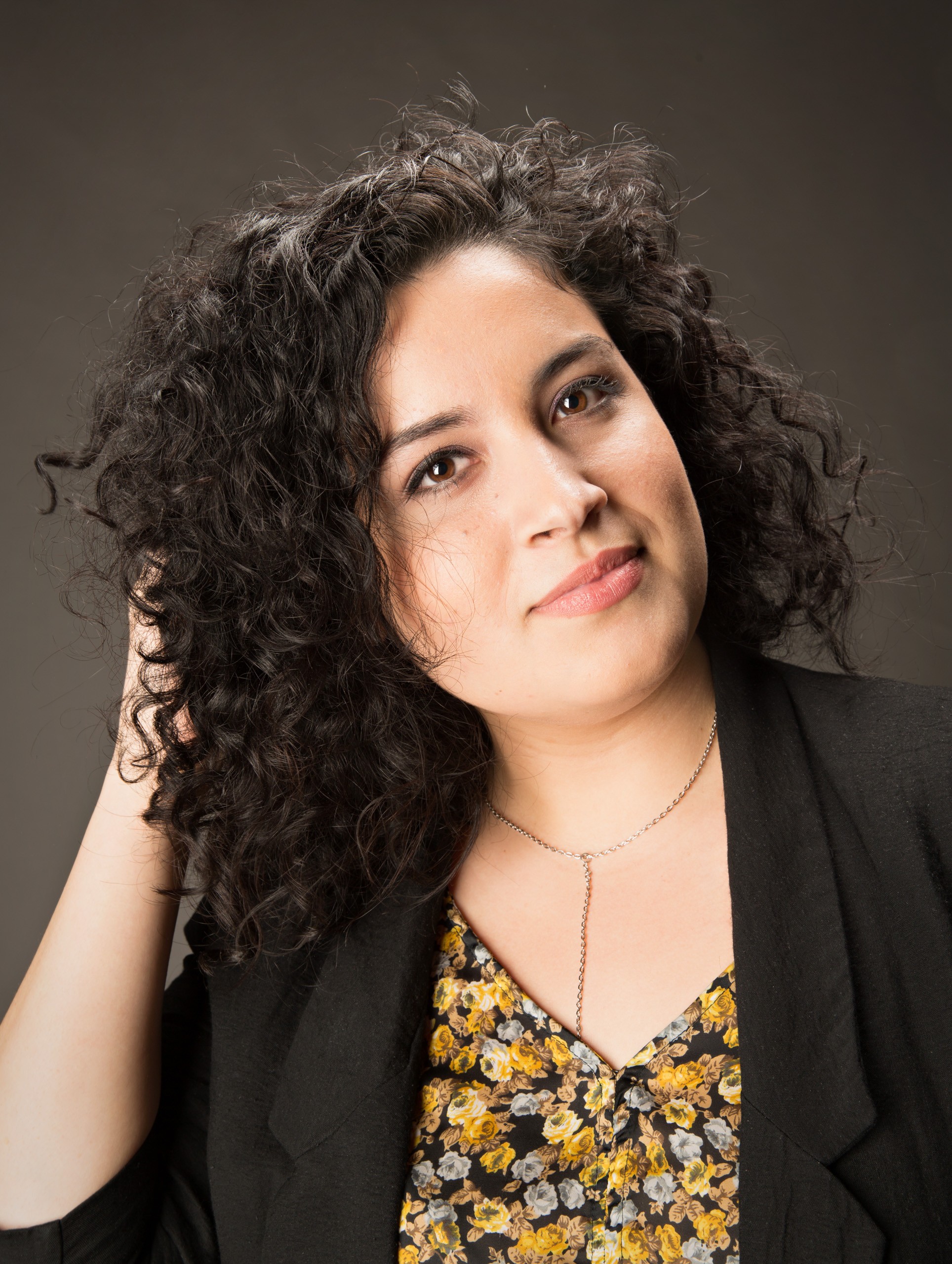 Professional headshot of woman with curly dark hair against neutral background