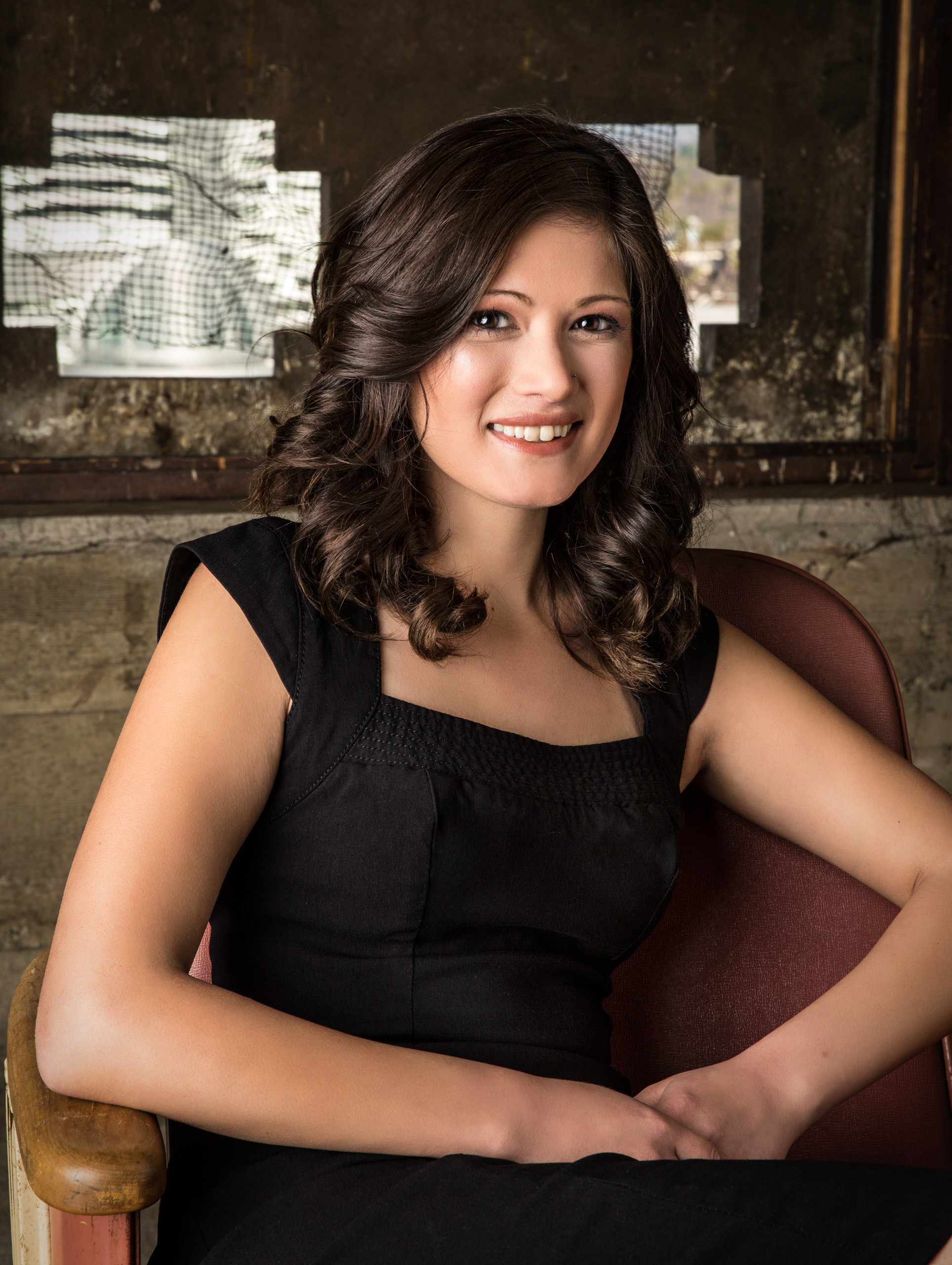 Professional portrait of smiling woman in black dress, industrial backdrop