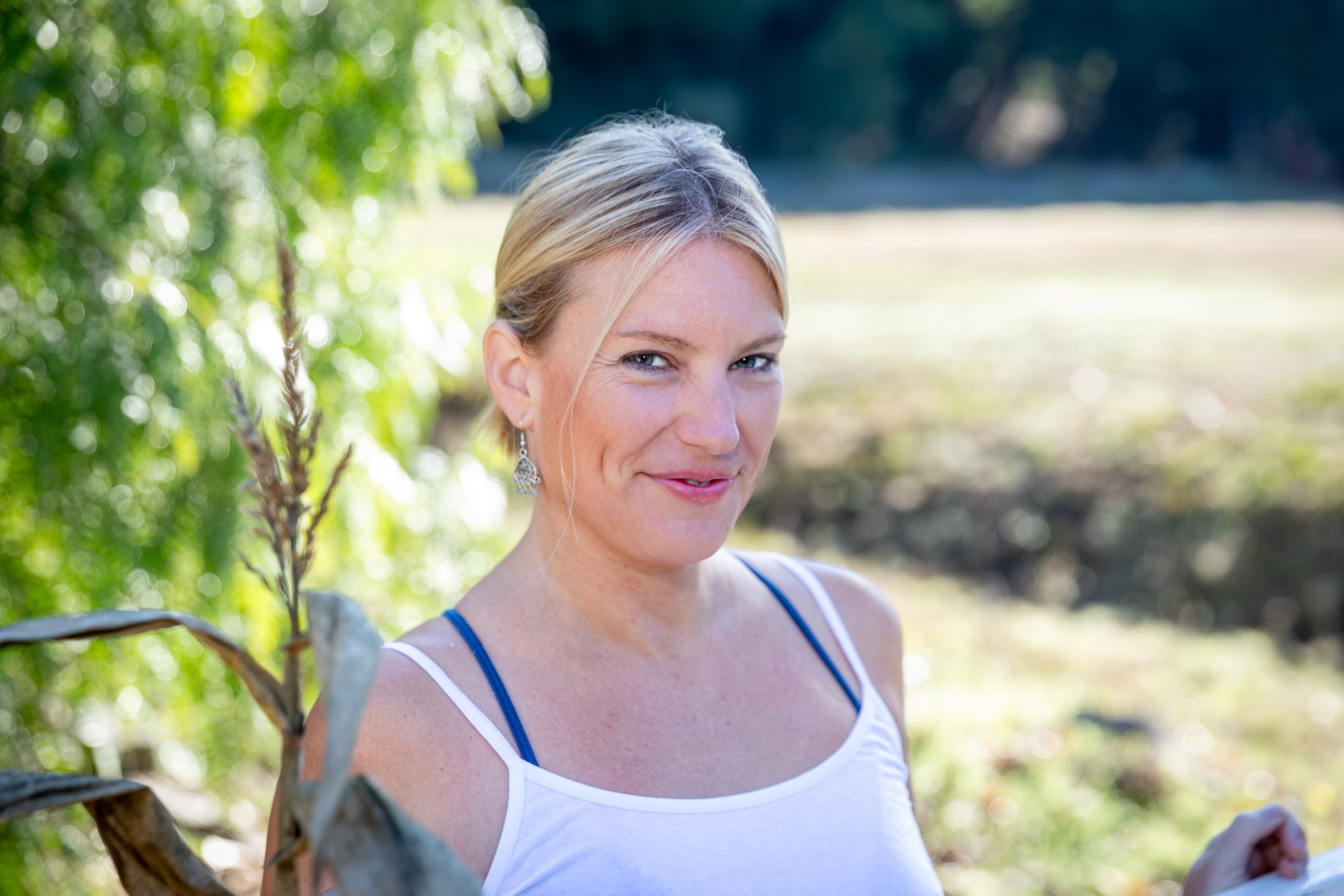 Woman smiling outdoors beneath hanging willow branches in natural light