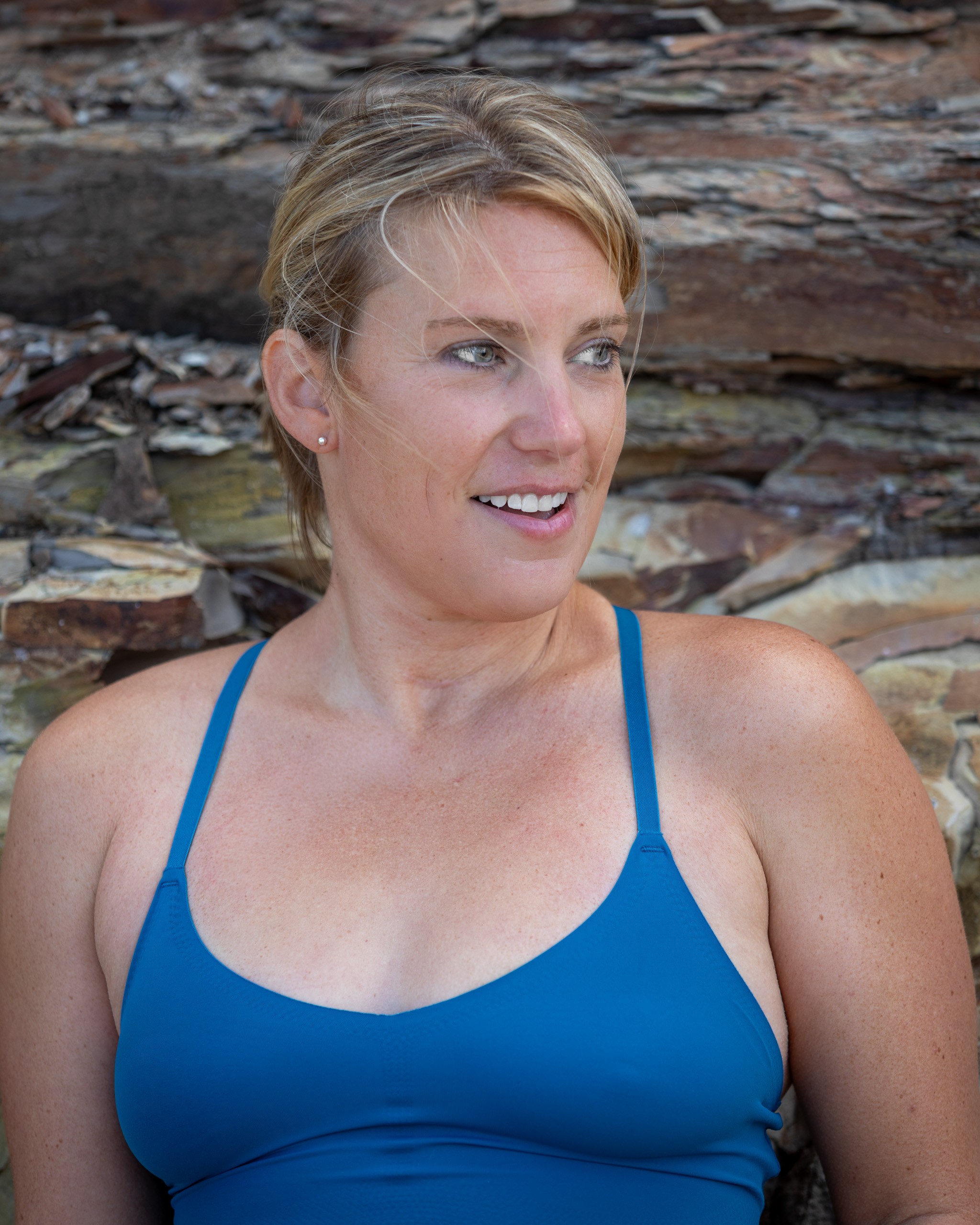 Woman in blue swimsuit smiling against rustic stone wall