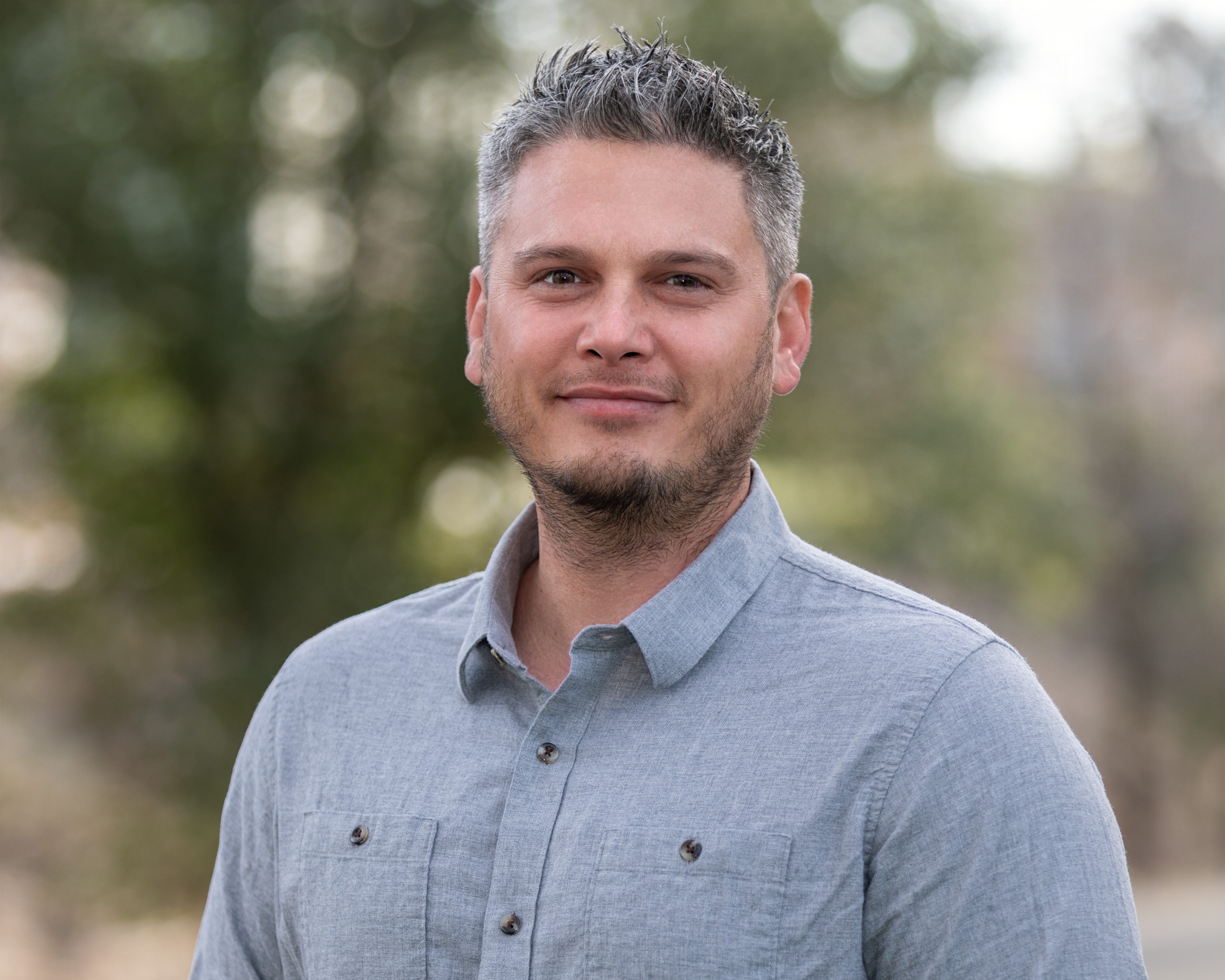Professional headshot of man in blue shirt outdoors