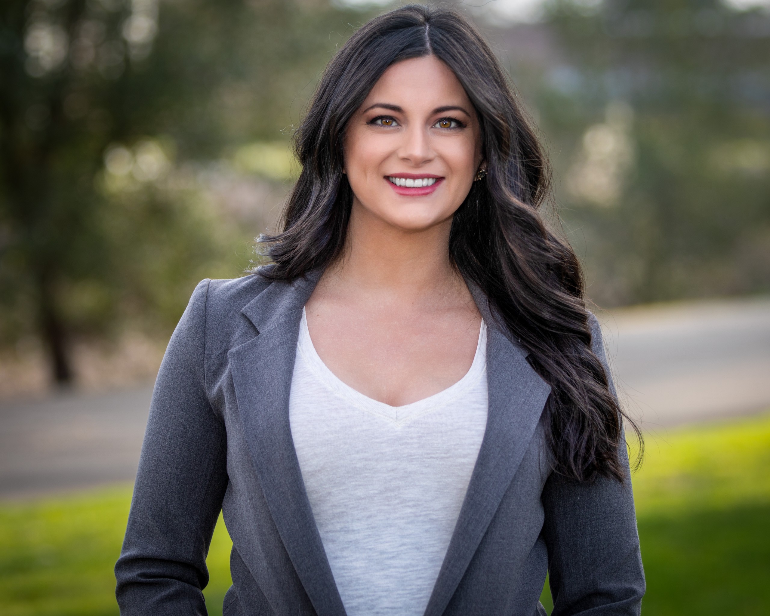 Professional headshot of smiling woman in gray blazer outdoors