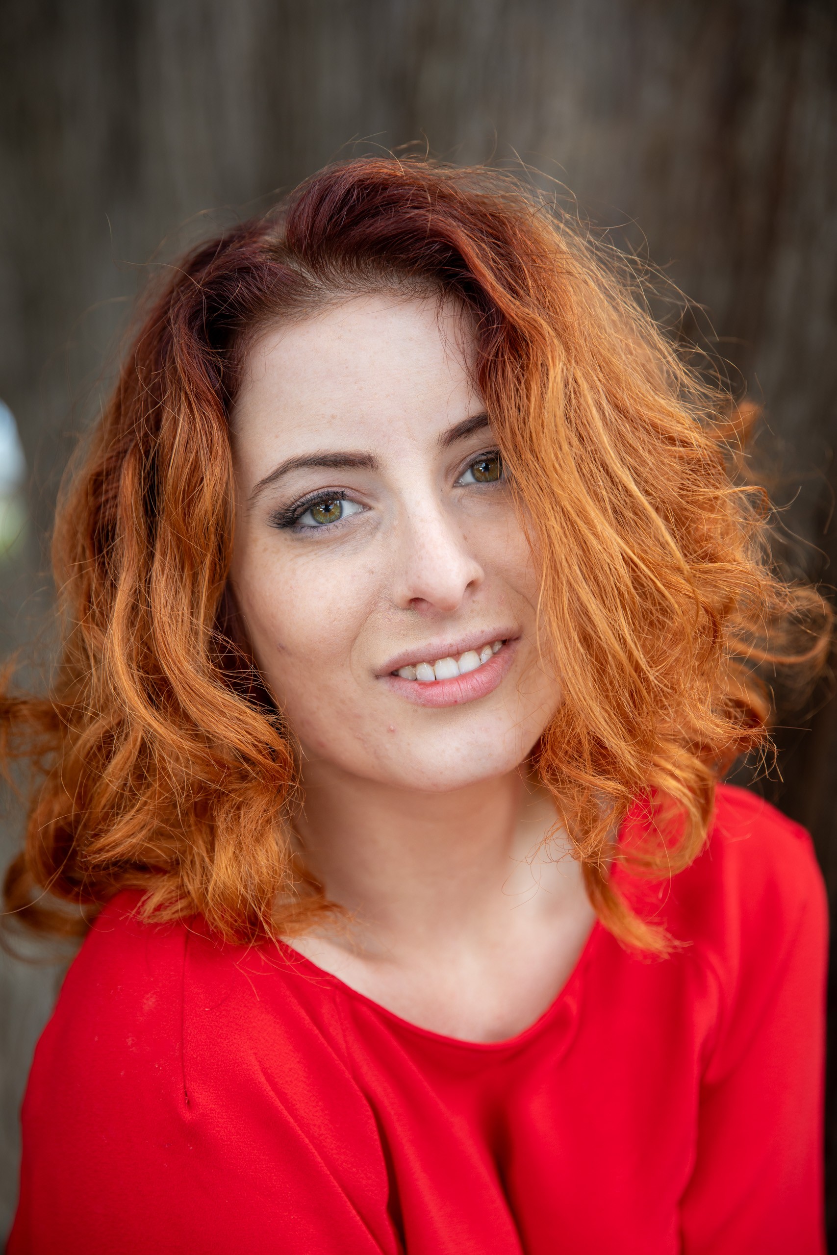 Woman with red curly hair smiling in bright red shirt