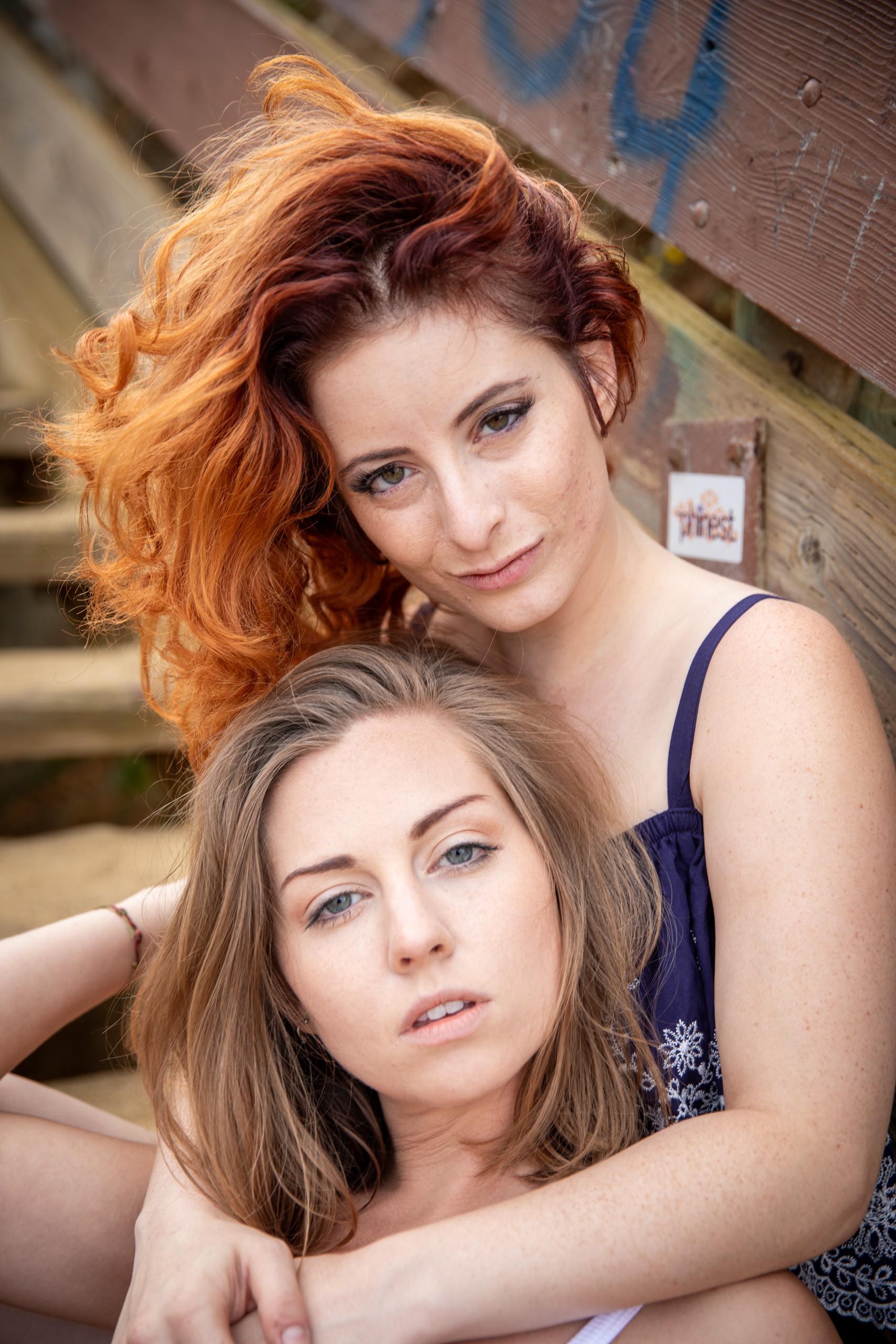 Two women posing together against an urban brick wall backdrop