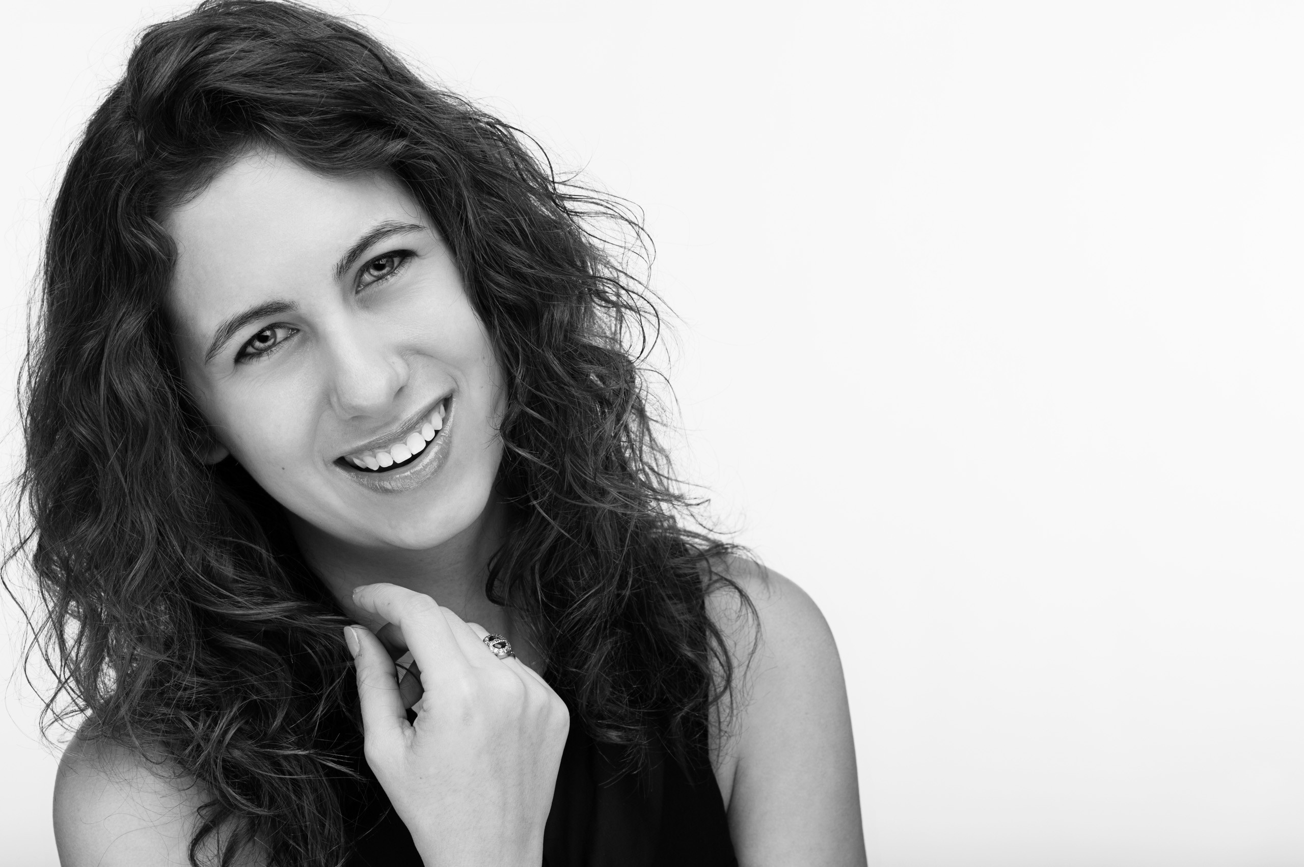 Woman with wavy dark hair smiling warmly against white background