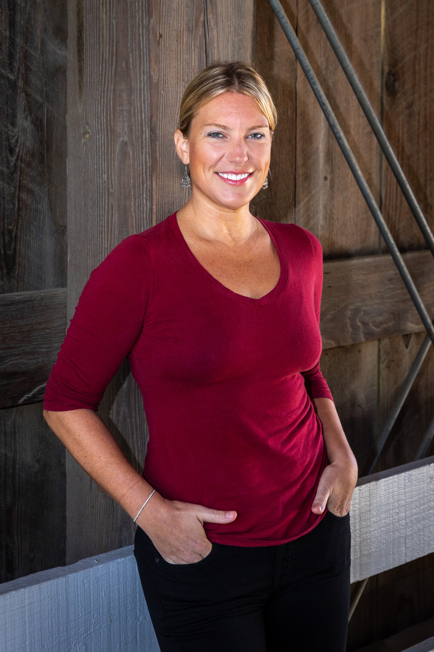 Pregnant woman in red top smiling against wooden backdrop