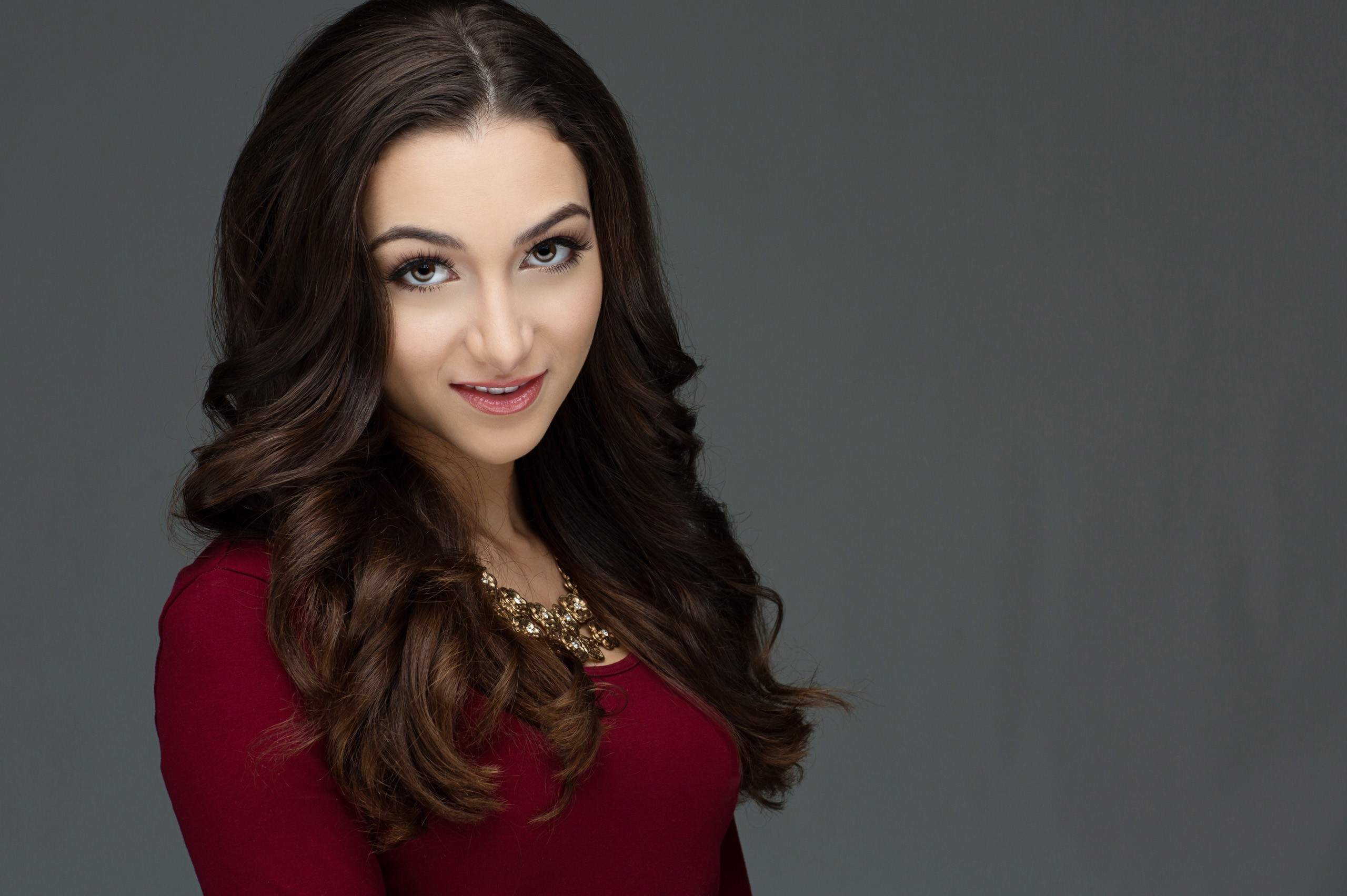 Professional headshot of woman in burgundy top against gray background