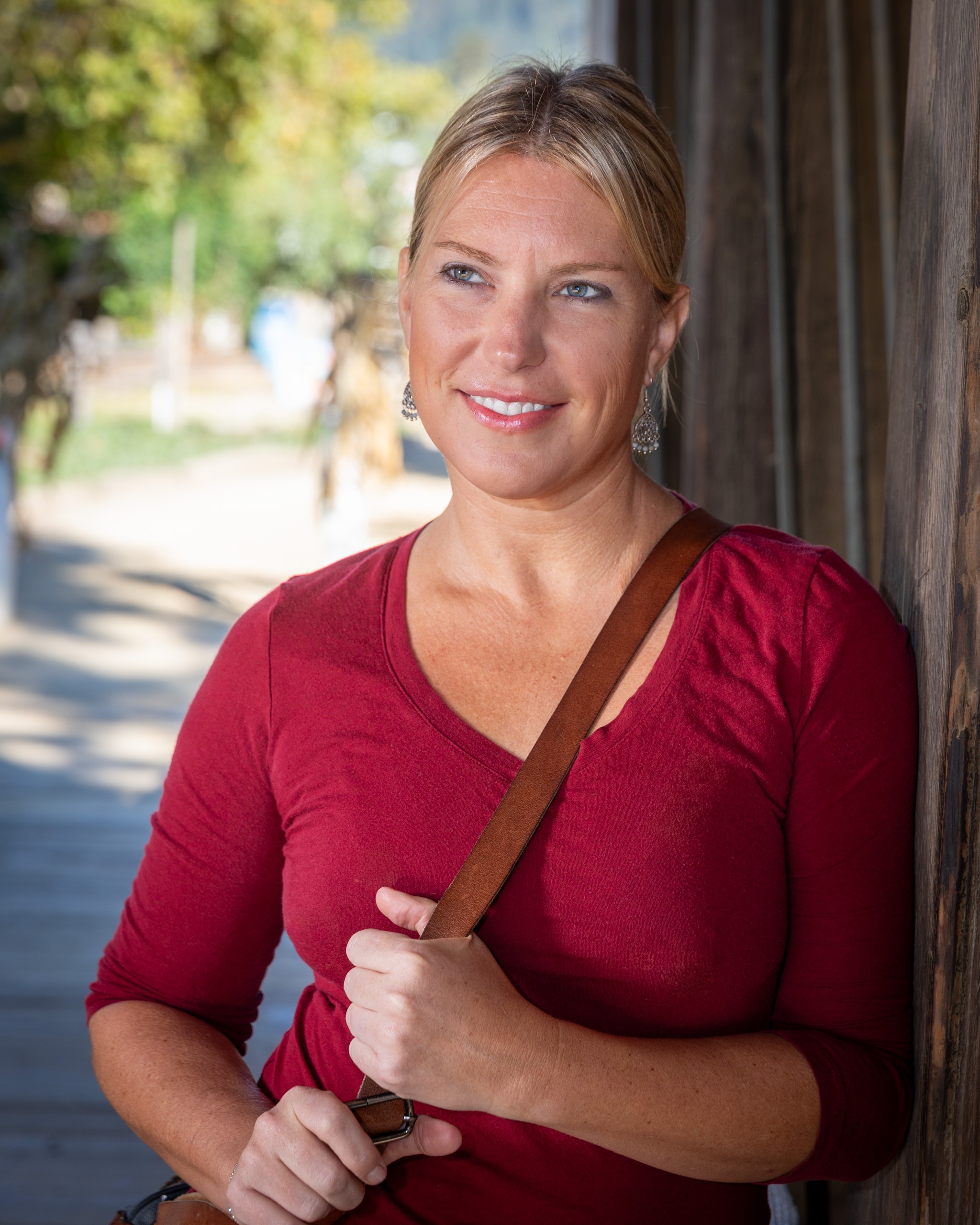 Woman in burgundy top smiling outdoors against wooden post